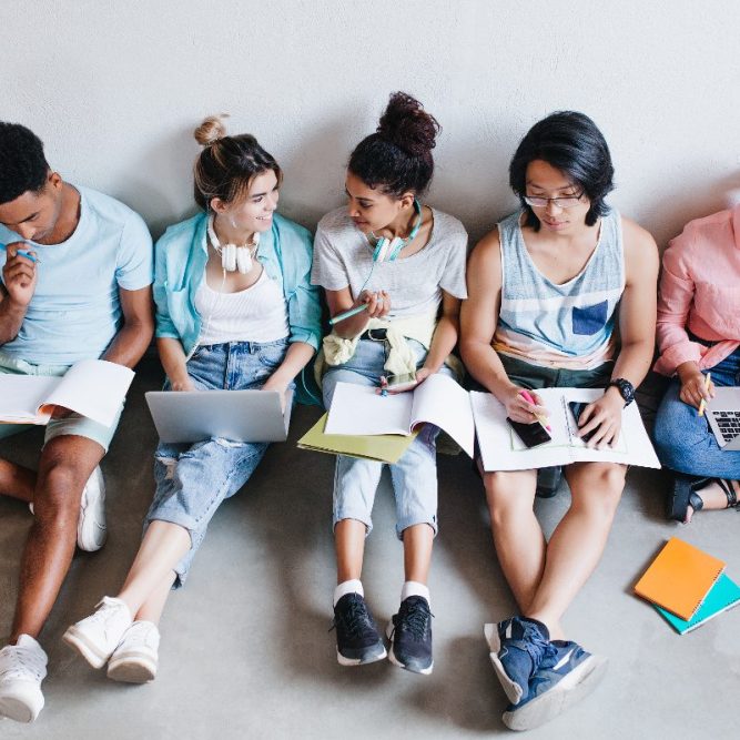 Overhead portrait of international students waiting for test in college. Group of university mates sitting on the floor with books and laptops, doing homework.